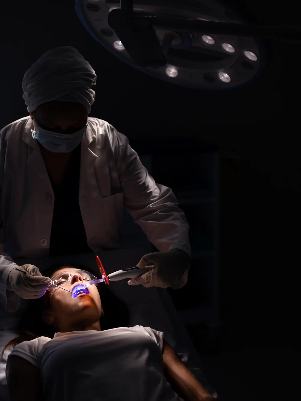 Zahnarzt behandelt eine Patientin im Behandlungsstuhl unter der Behandlungsleuchte